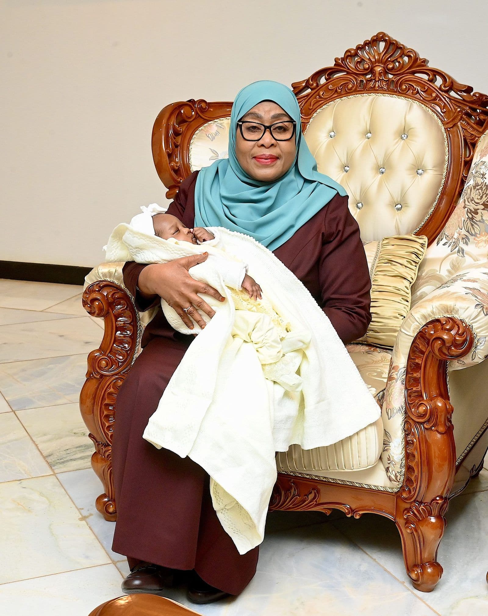 H.E. Dr. Samia Suluhu Hassan seated in an armchair holding a newborn