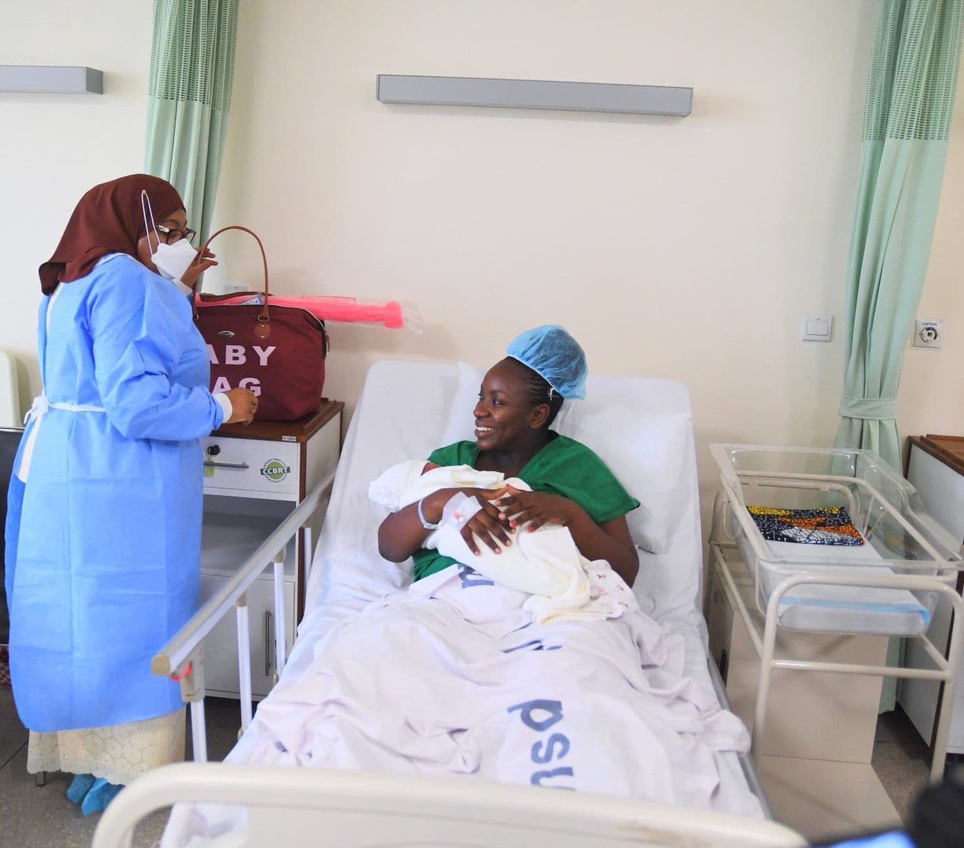 The President in a surgical gown beside a hospital bed where a mother holds her newborn