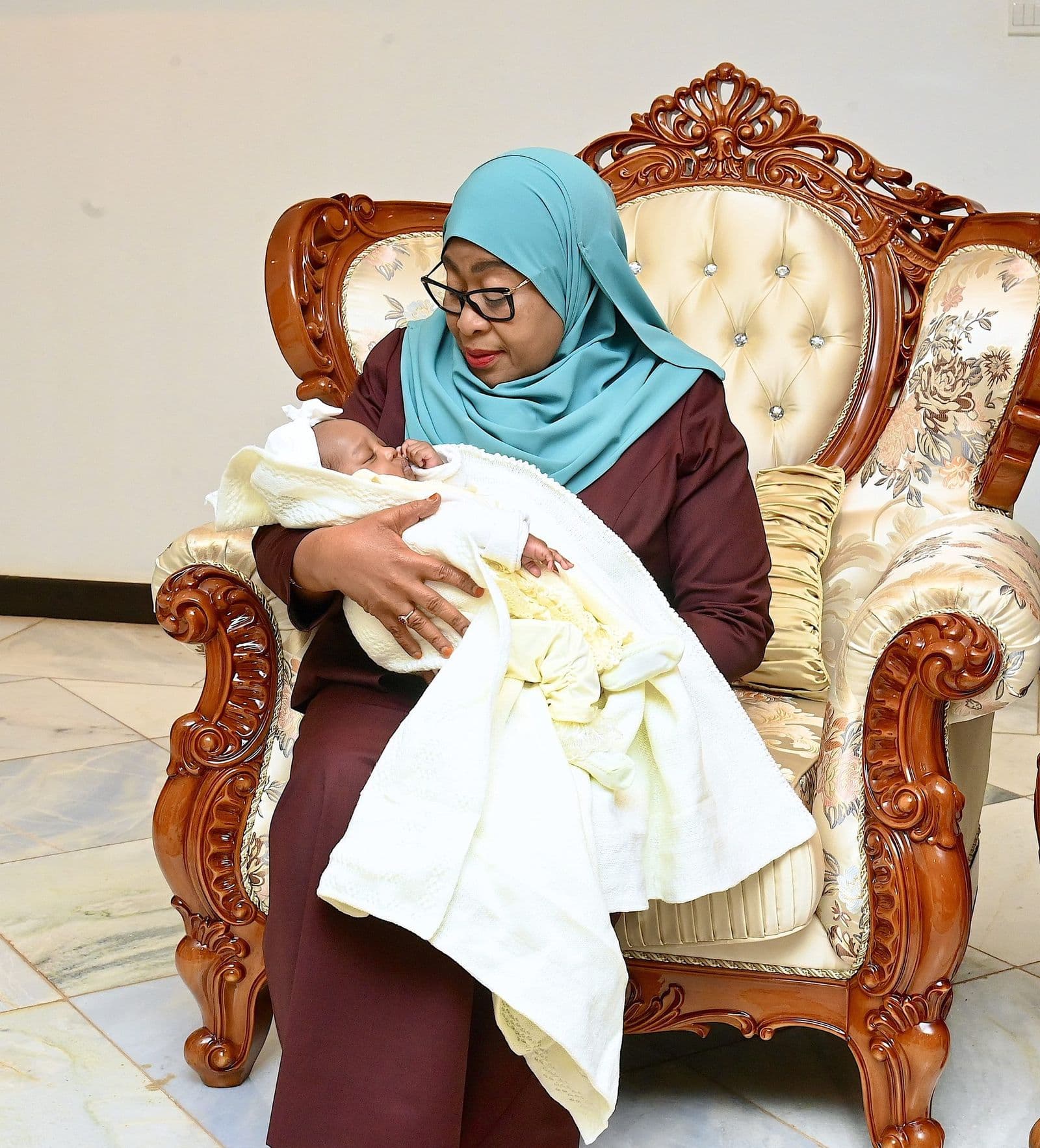 H.E. Dr. Samia Suluhu Hassan seated, holding a newborn wrapped in a white shawl